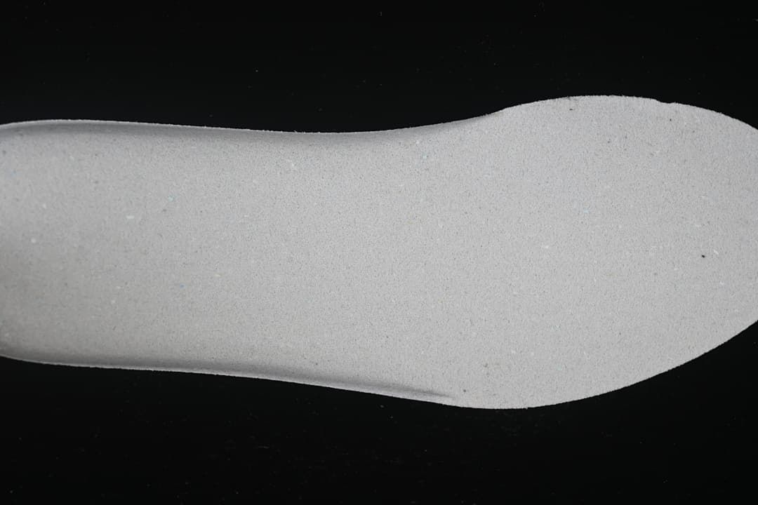 Close-up of a light-colored shoe component against a dark background.