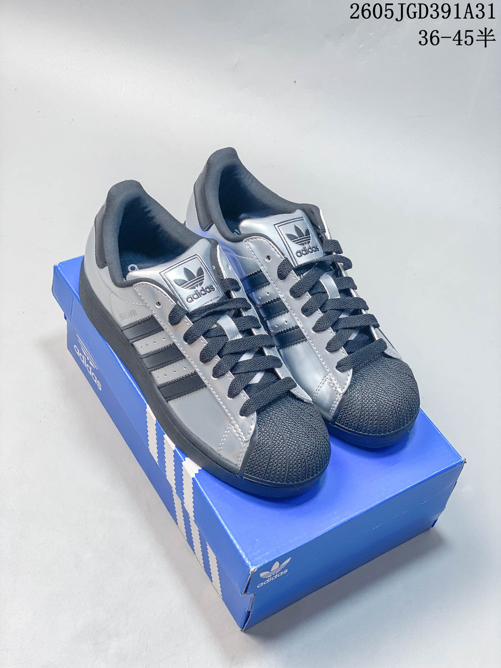 Pair of silver Adidas Superstar sneakers with dark shell toes and dark laces on a blue shoe box.
