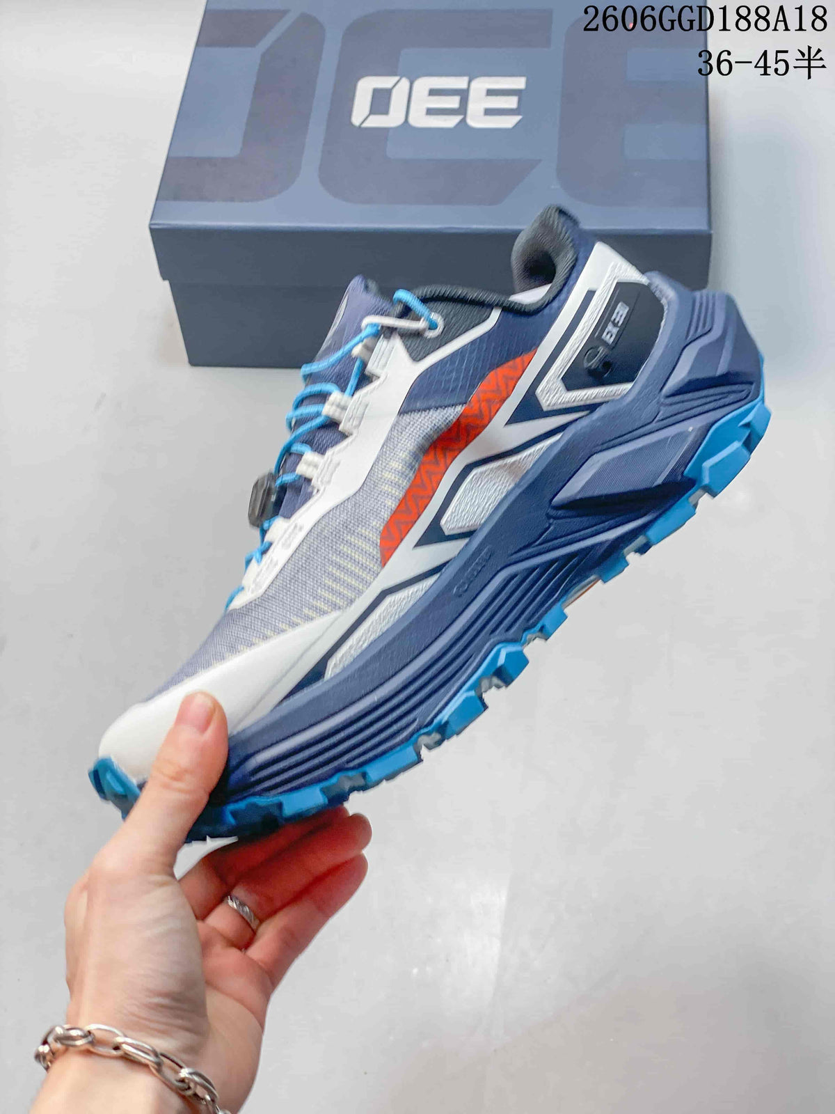 Side view of the gray, navy, and orange trail shoe with blue outsole lugs