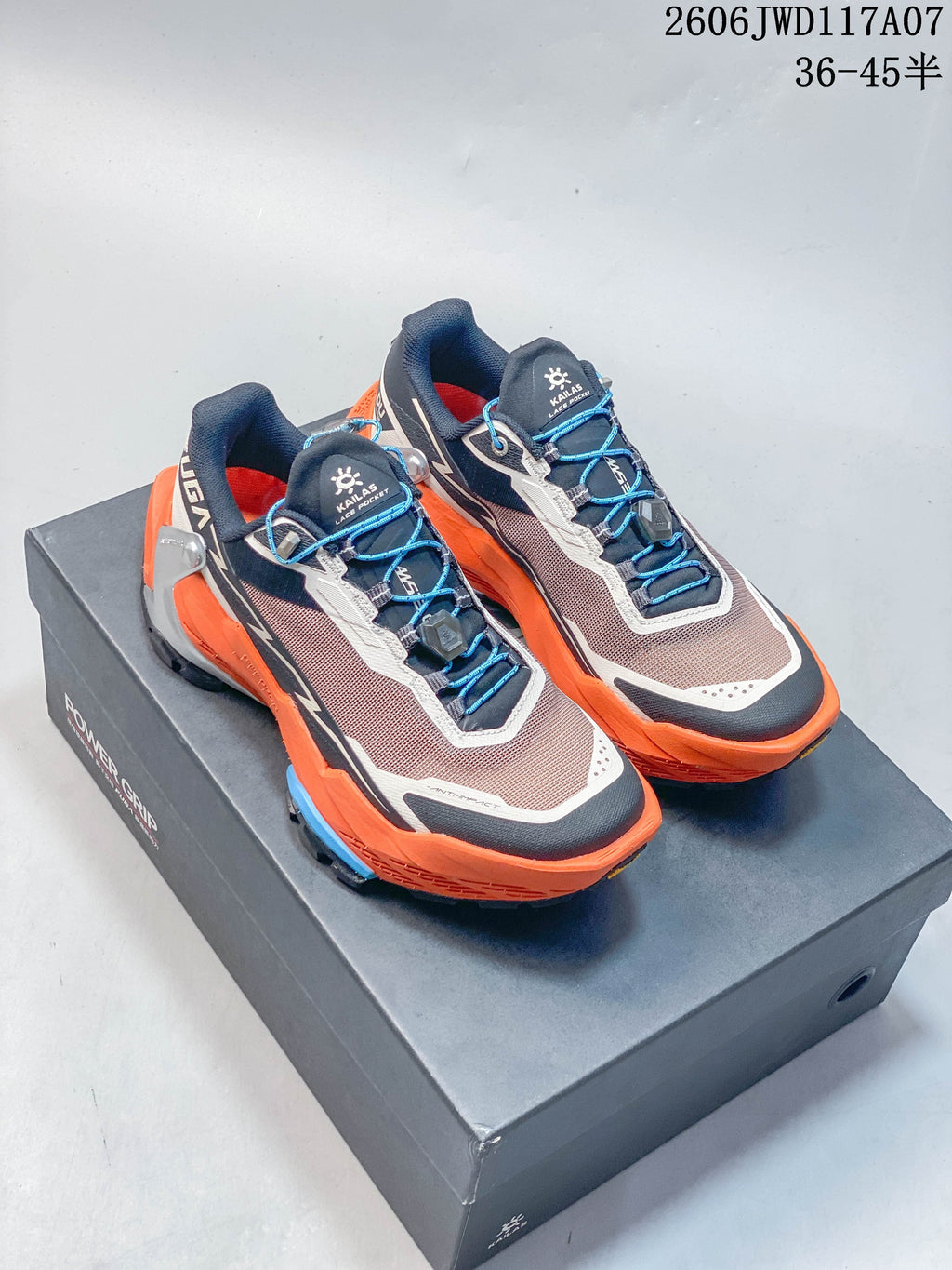 Pair of Kailas Fuga DU 2 trail running shoes in orange, grey, navy and blue, shown on a shoe box.