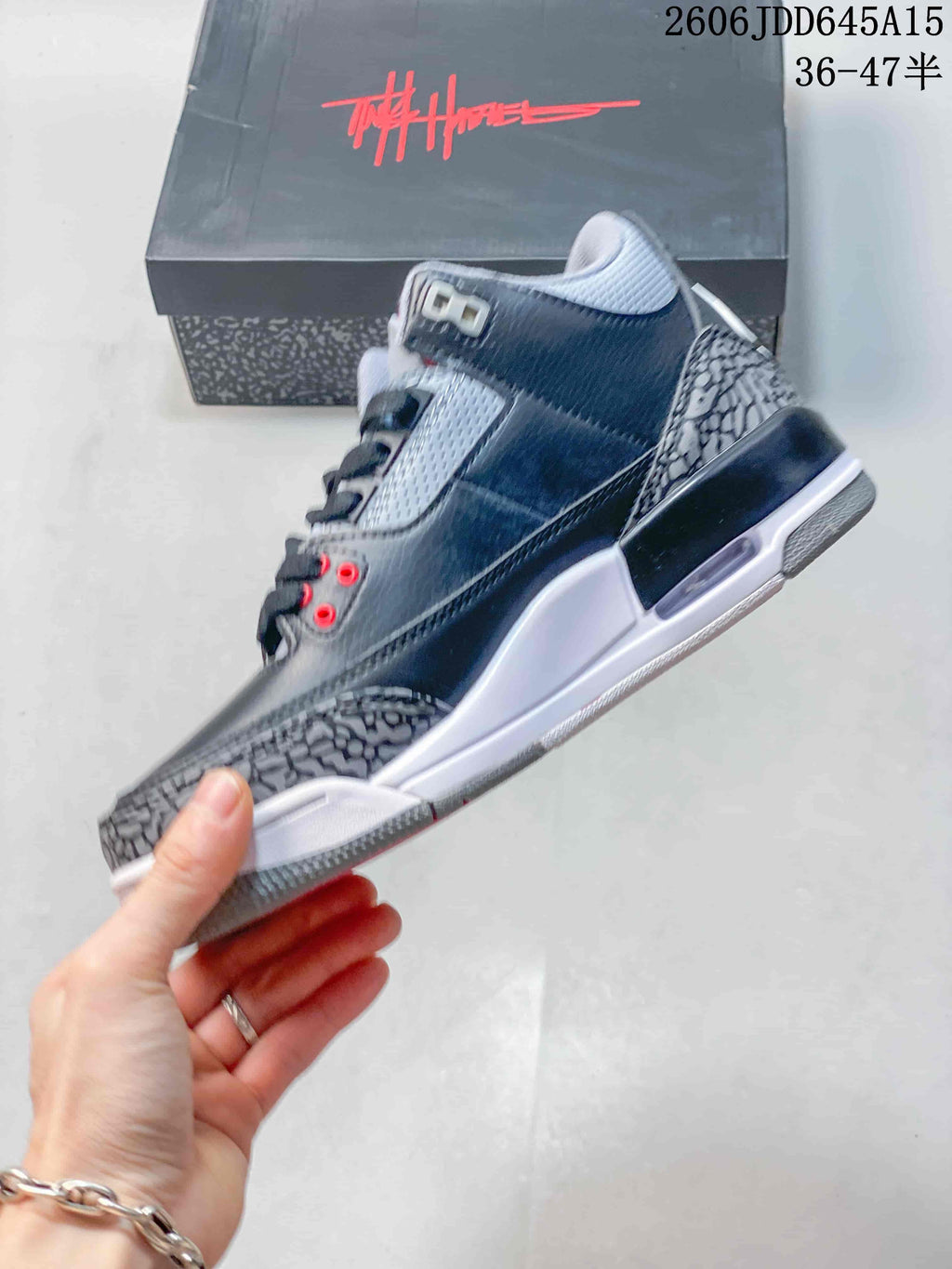 Side view of a grey mid-top sneaker with elephant-print overlays and red lace-eyelet accents.