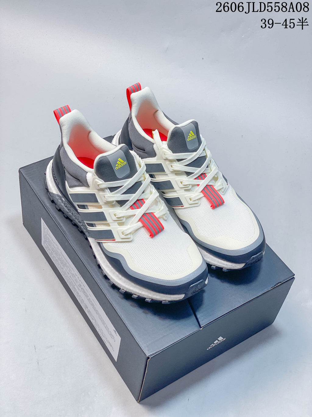 Pair of white, grey and navy Adidas sneakers with red accents displayed on a shoebox.