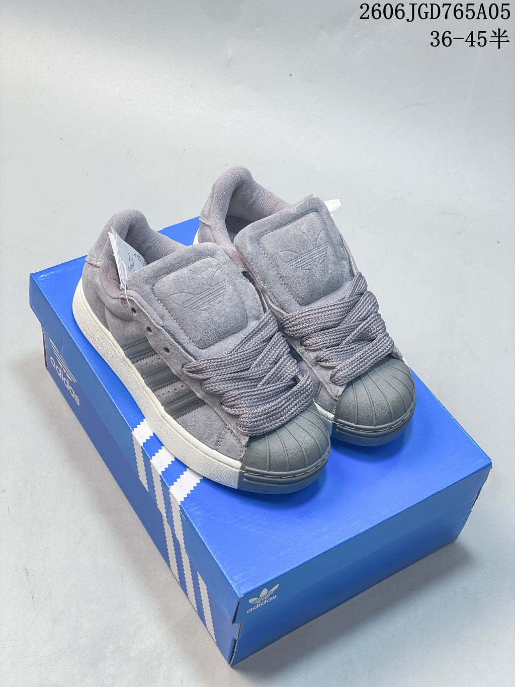 Pair of grey Adidas Originals Superstar XLG sneakers photographed on a blue shoe box.