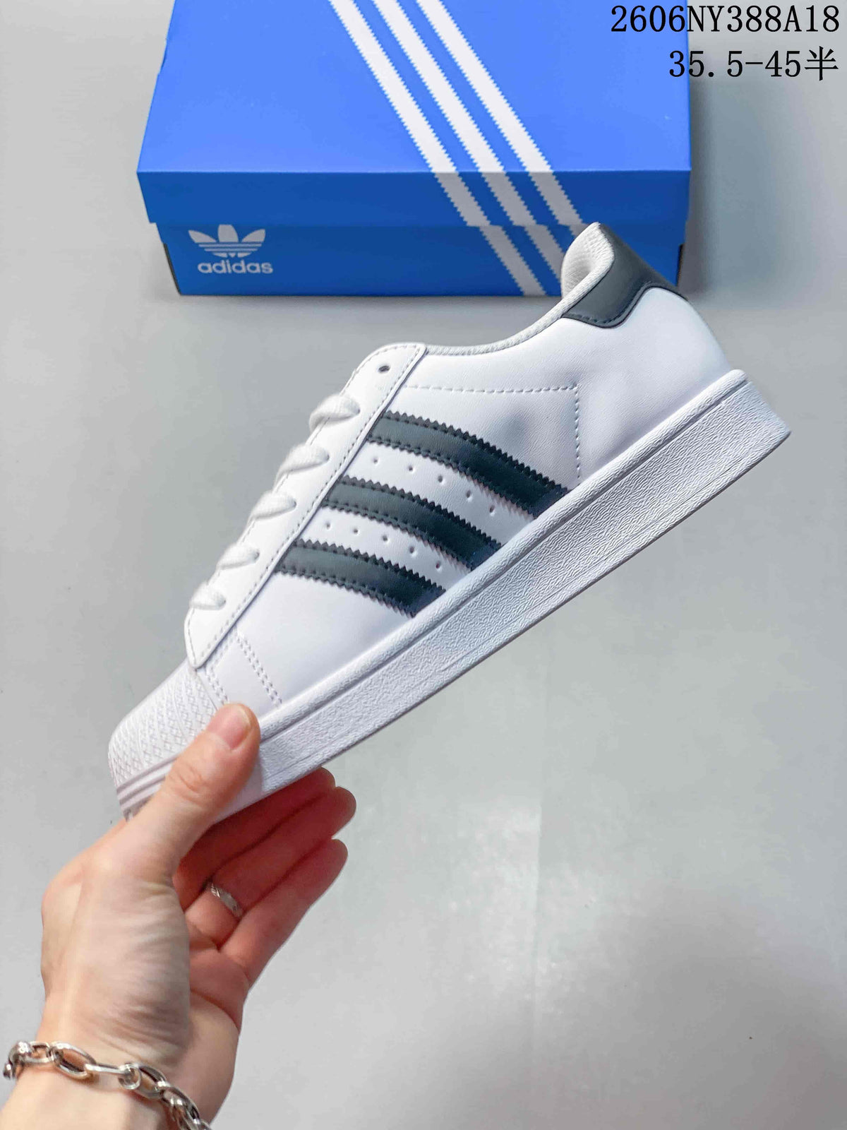 Side profile of a white Superstar sneaker with charcoal stripes and a flat sole