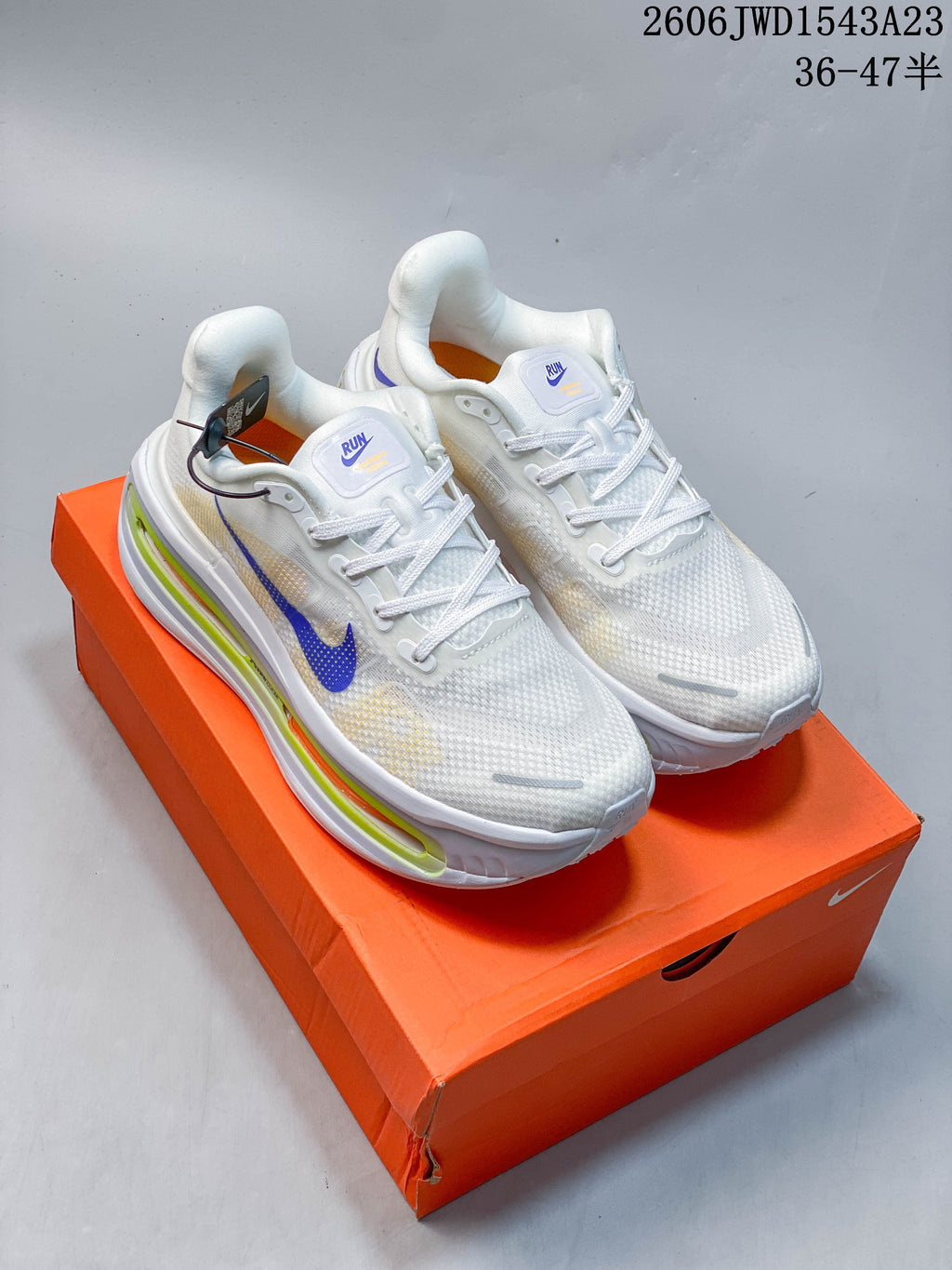 Pair of white Nike Vomero Premium running shoes with blue, lime, and orange accents on an orange shoebox