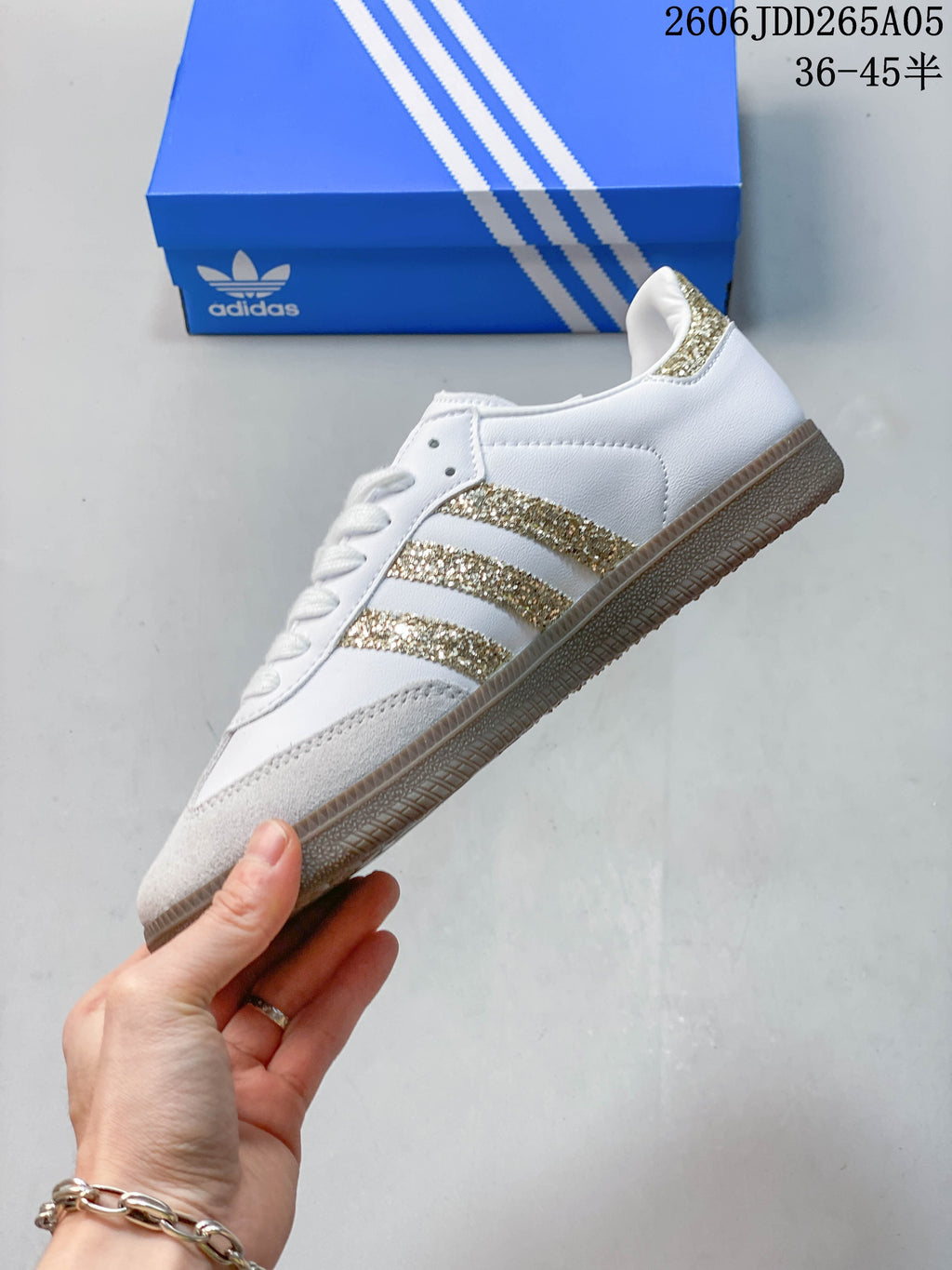 Side view of a white low-top sneaker with gold glitter stripes, suede-look toe overlay, and gum-colored outsole.
