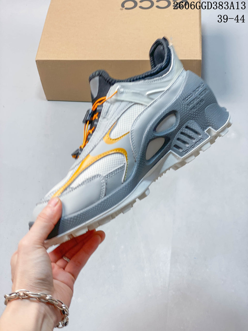 Side view of the sneaker with orange accents, gray panels, and a chunky treaded sole.