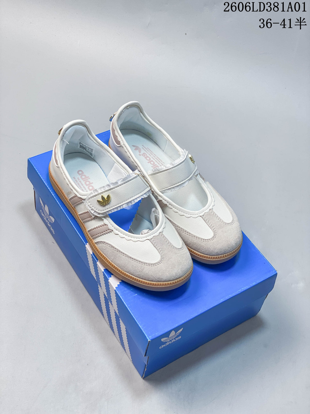Pair of white and pale neutral Adidas Samba Jane Mary Jane-style sneakers with strap closures and gum-colored soles, shown on a blue shoebox.