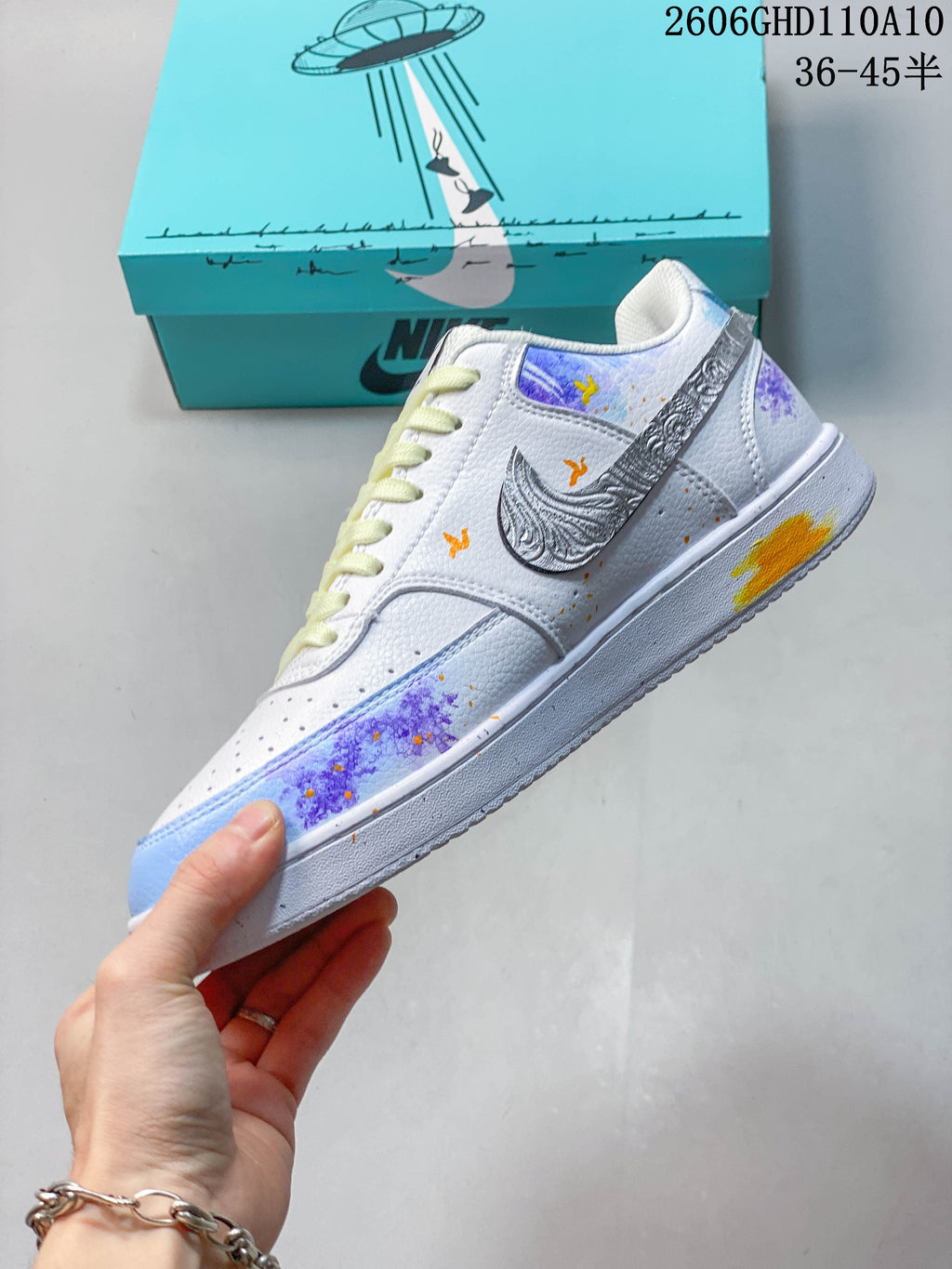 Side view of a white low-top sneaker with colorful decorative artwork and a silver-toned patterned side logo.