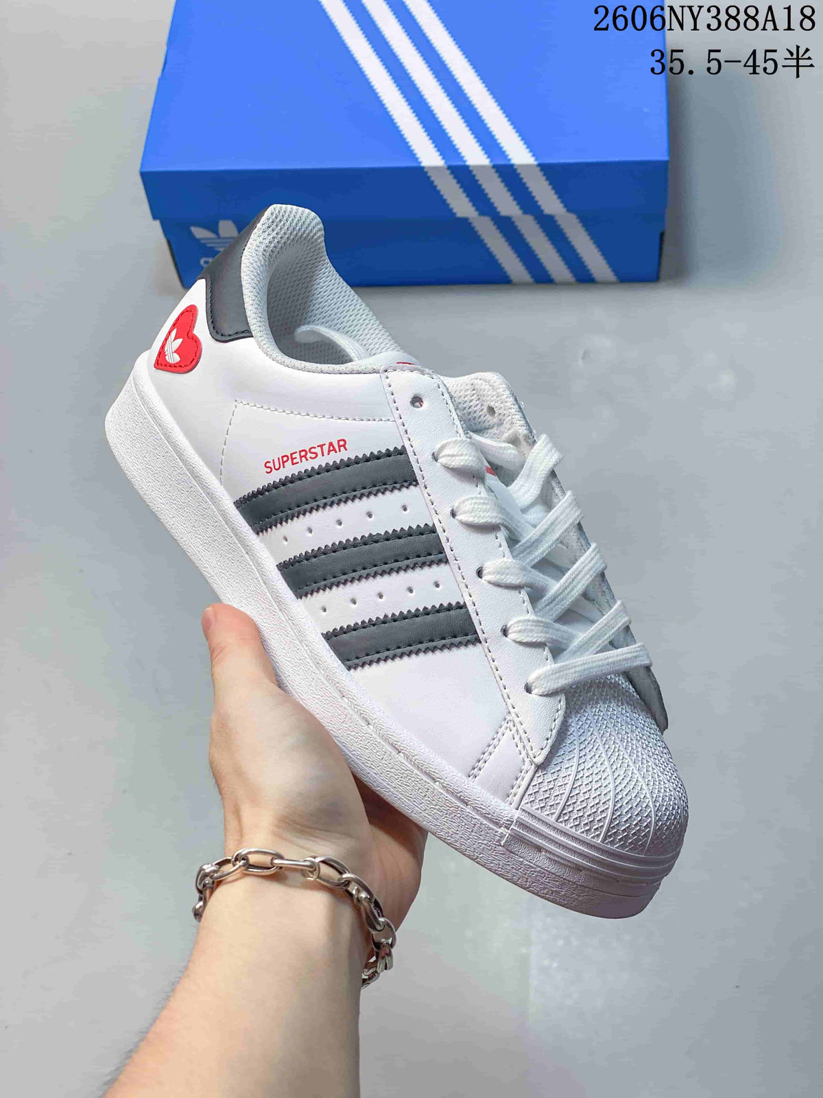 Close-up of a white Adidas Superstar sneaker with dark side stripes and a red heel accent.