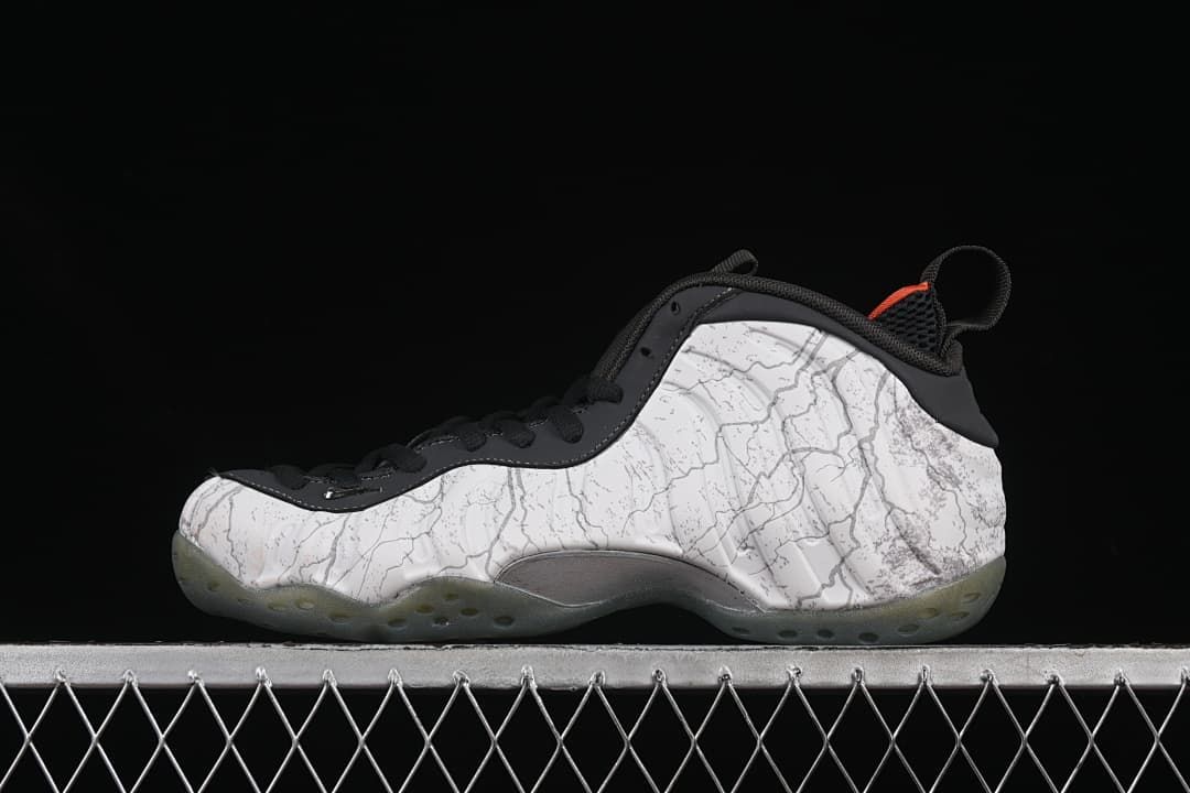 Side view of the white and gray patterned sneaker with black trim and orange accents.