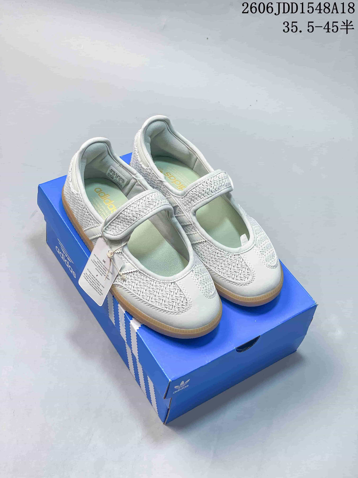 Pair of white Adidas Samba Jane-style sneakers with woven-look panels, instep straps, and gum-colored soles.