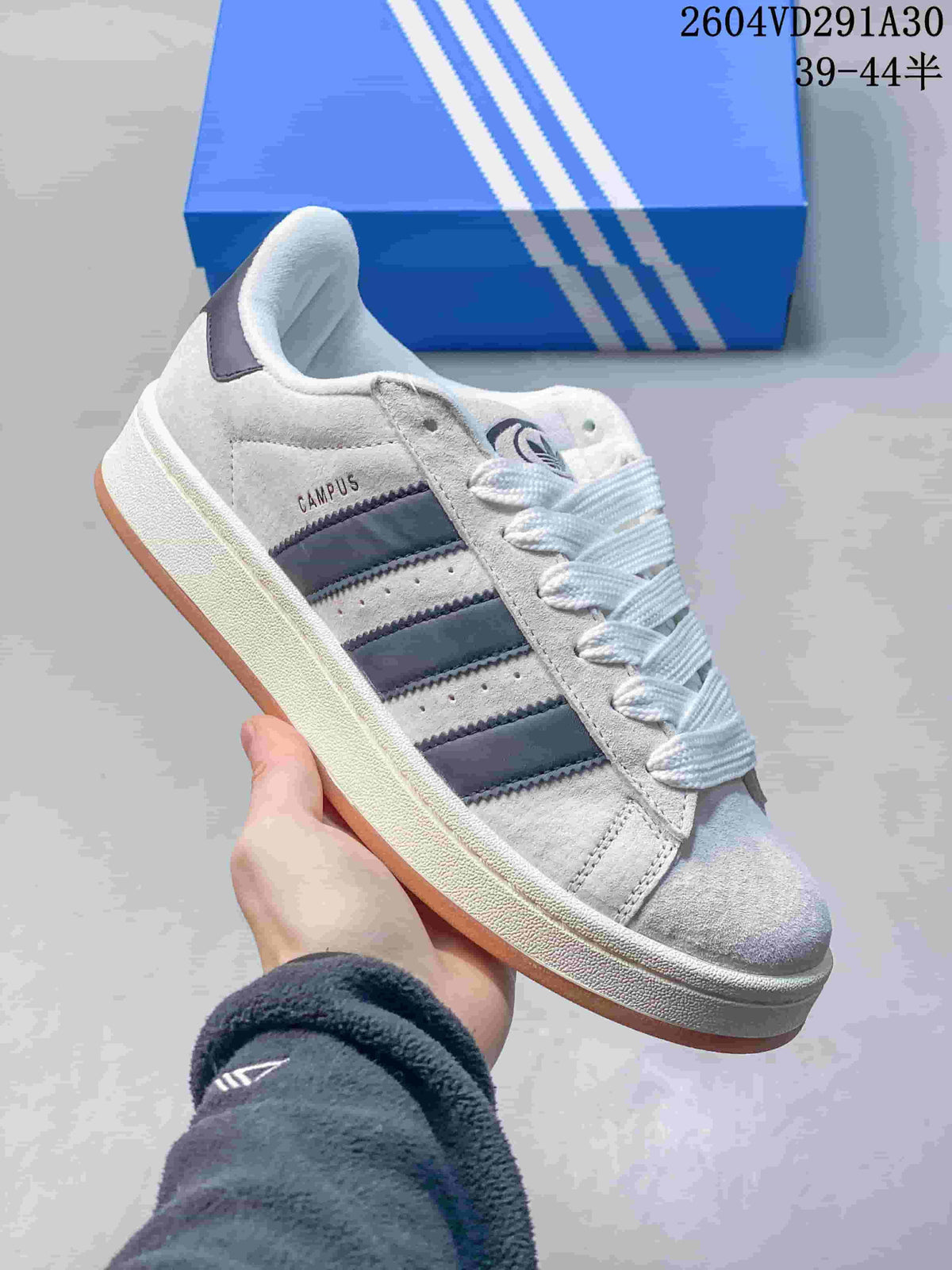 Close view of a light grey Adidas Campus sneaker with dark stripes and gum-colored outsole.