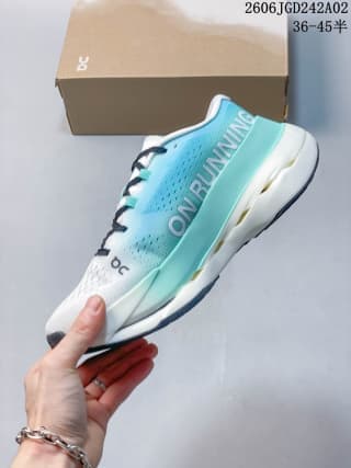 Side view of turquoise and white ON Cloudboom Max sneakers held in front of a shoe box, with the style code and EU size range visible above.