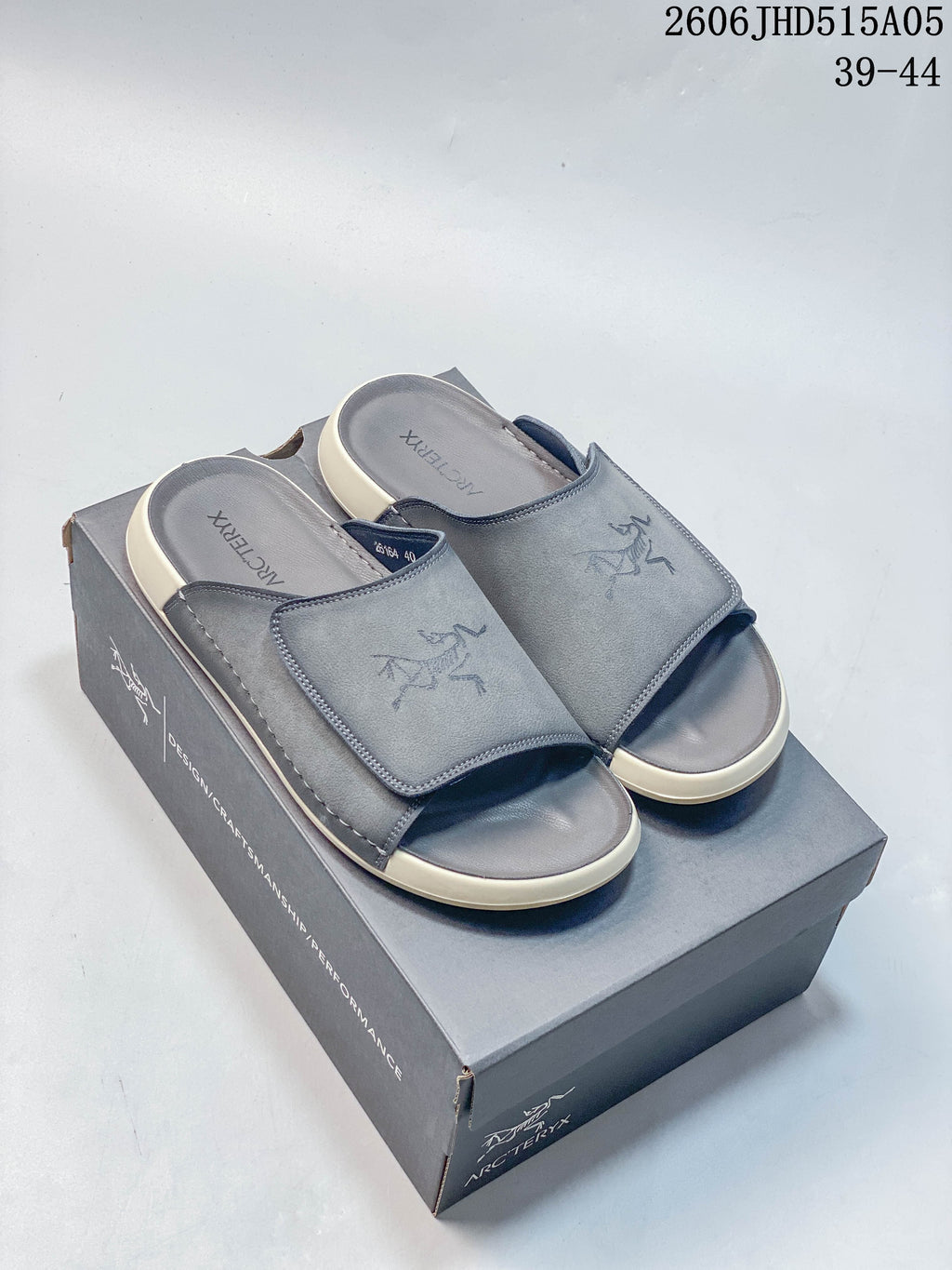 Pair of gray open-toe slide sandals with wide straps, shown on a branded box.