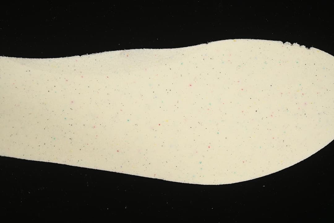Close-up of a light-colored shoe component with small multicolor flecks.