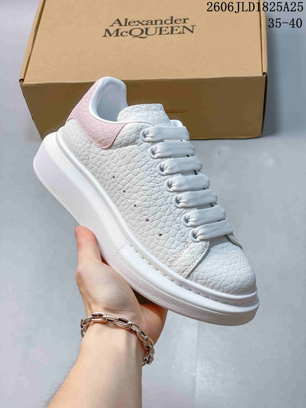Side view of a white textured sneaker with pale pink heel panel, thick sole, and a branded box.