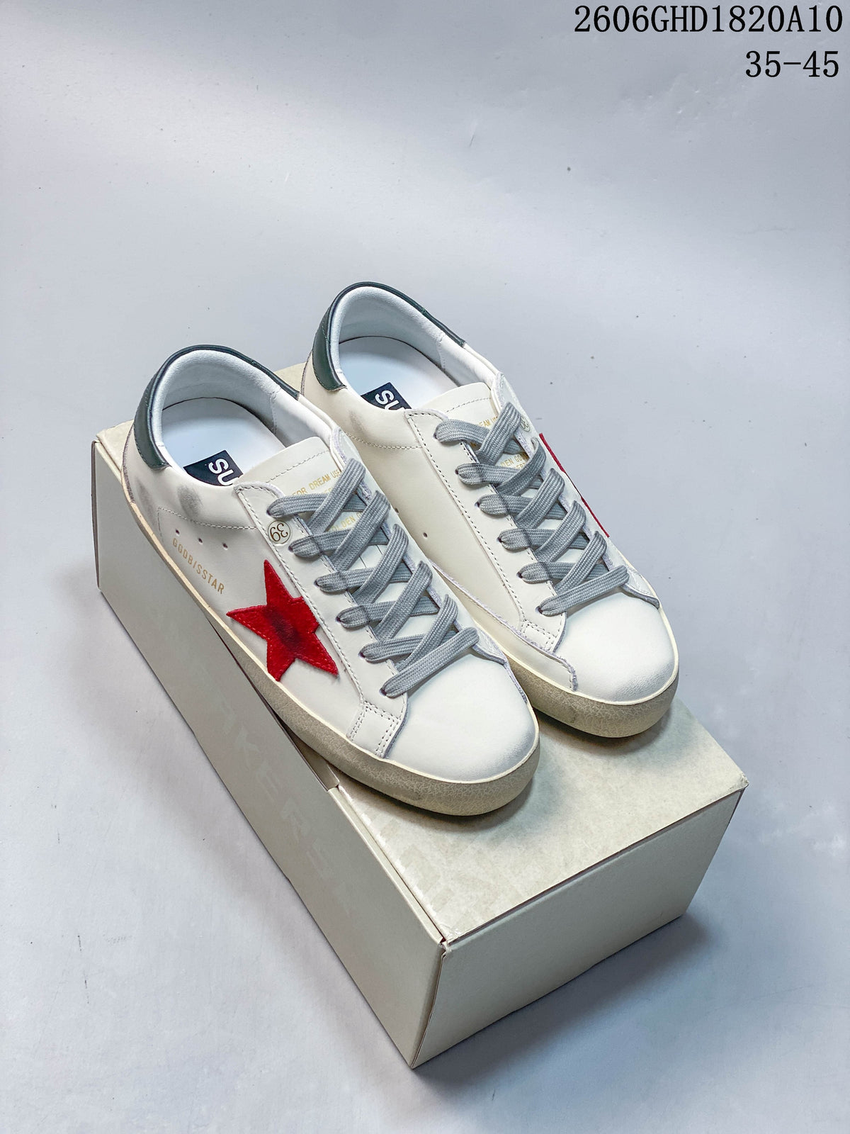 Pair of white low-top sneakers with red star details, gray laces, and dark green heel tabs on a box.