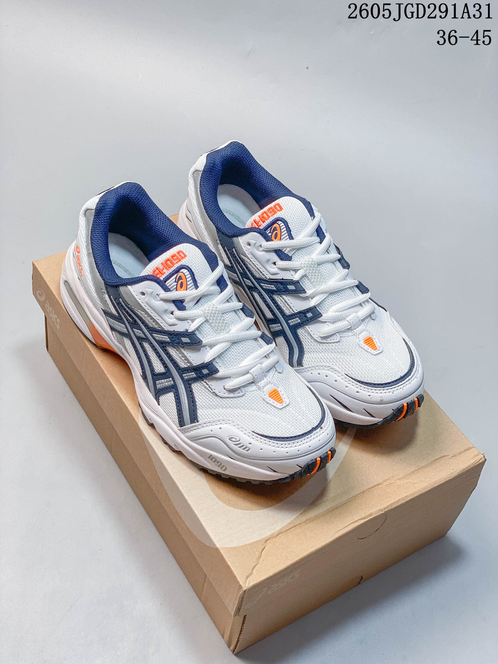 Pair of white ASICS sneakers with navy overlays and orange accents, shown on a box.