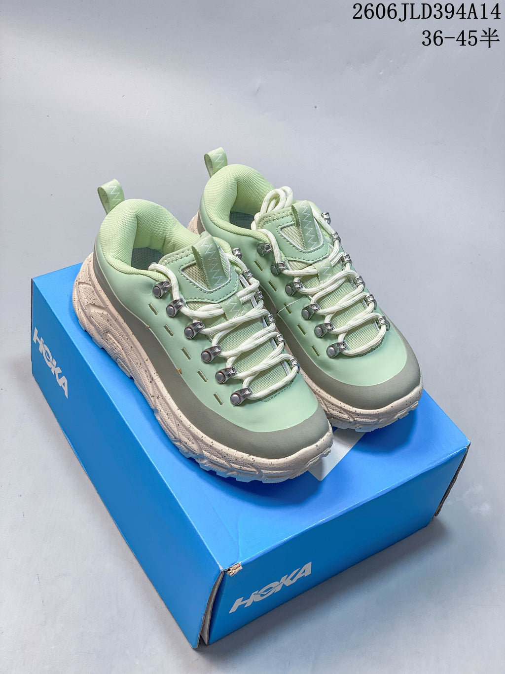 Pair of mint-green and gray HOKA low-top sneakers on a blue shoe box