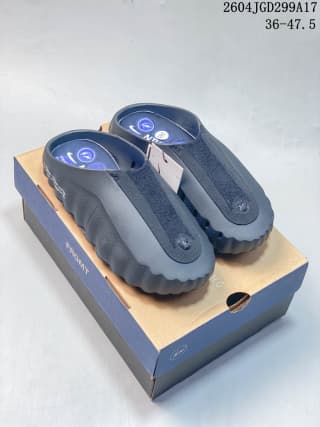 Dark gray Nike Mind slides displayed on a blue and tan box, with circular footbed nodes visible.