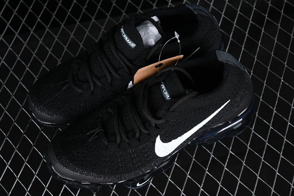 Pair of black sneakers with white Swooshes shown from above.
