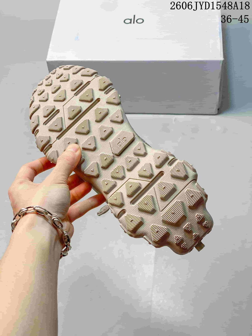 Close-up of the shoe's lugged outsole with an Alo logo box in the background.