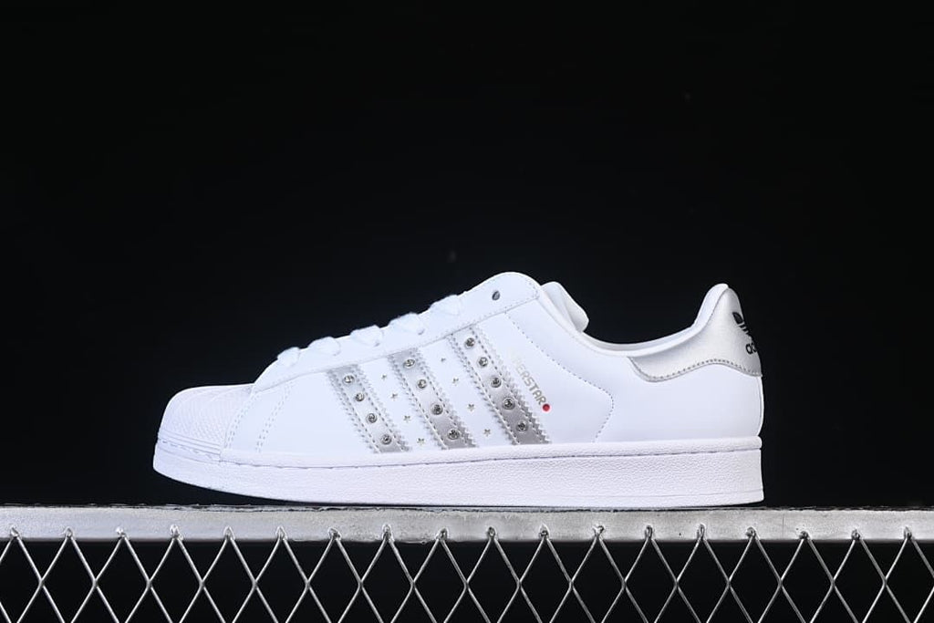 Side view of a white adidas Superstar II sneaker with silver accents and decorative studded stripes