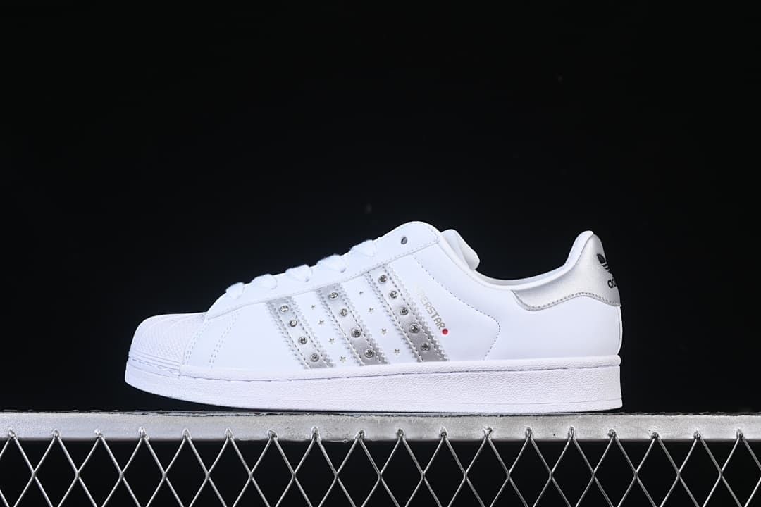 Side view of a white adidas Superstar II sneaker with silver accents and decorative studded stripes