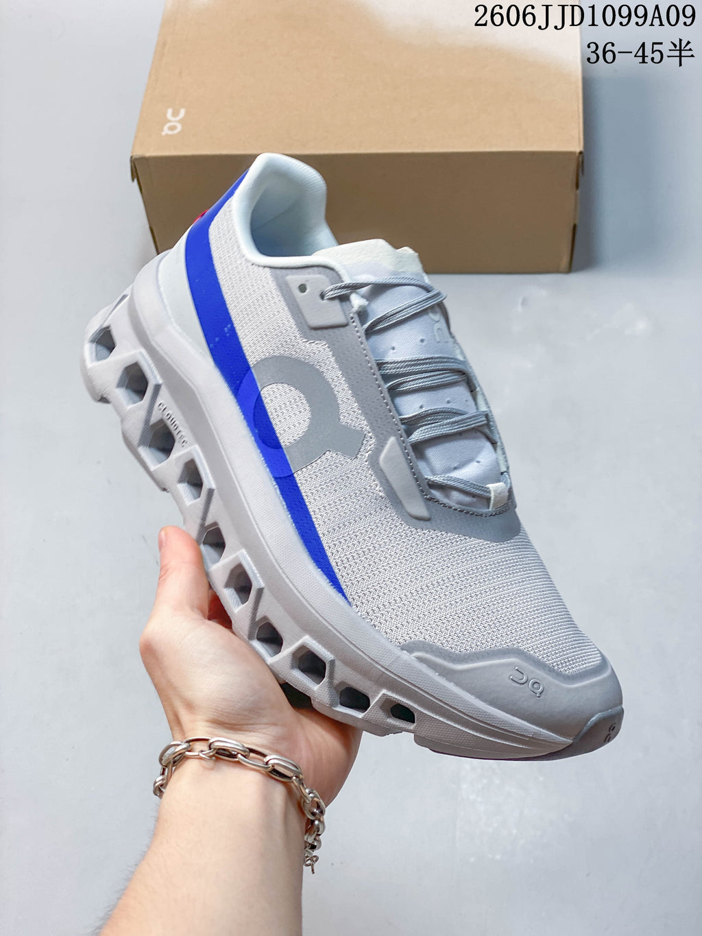Side view of a white and gray On Cloudmonster Void shoe with a blue accent stripe and sculpted sole.