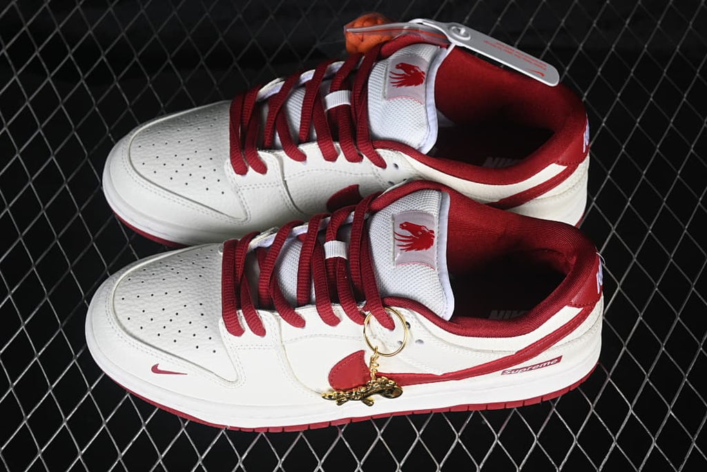 Pair of off-white and red Nike SB Dunk Low sneakers with horse-themed tongue graphics and a gold-tone charm
