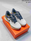 Nike running shoes in white, gray, dark navy and gold, shown on an orange shoe box.