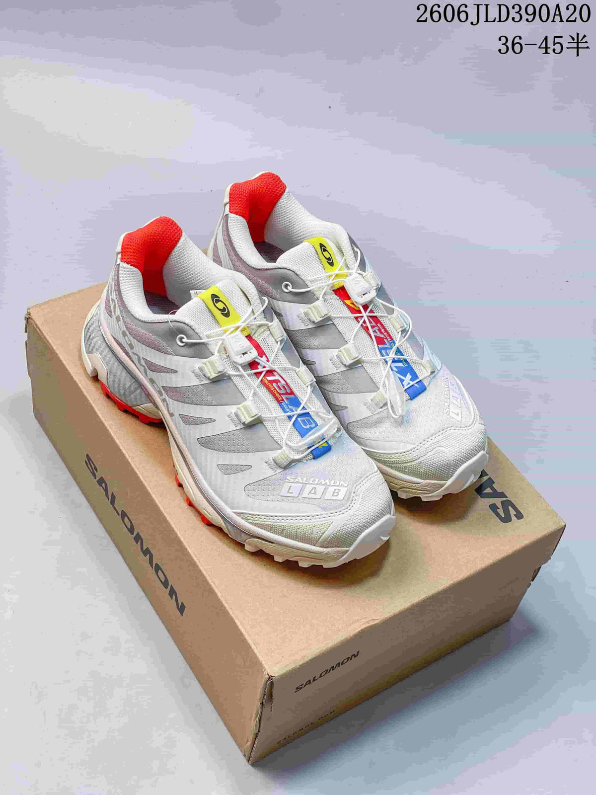 Pair of white and gray Salomon XT-4 OG shoes with red accents, shown on a branded shoe box.
