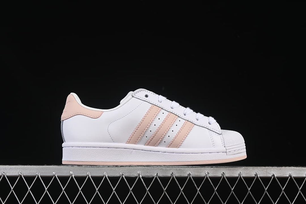 Side profile of the white sneaker with blush-pink stripes and heel panel.
