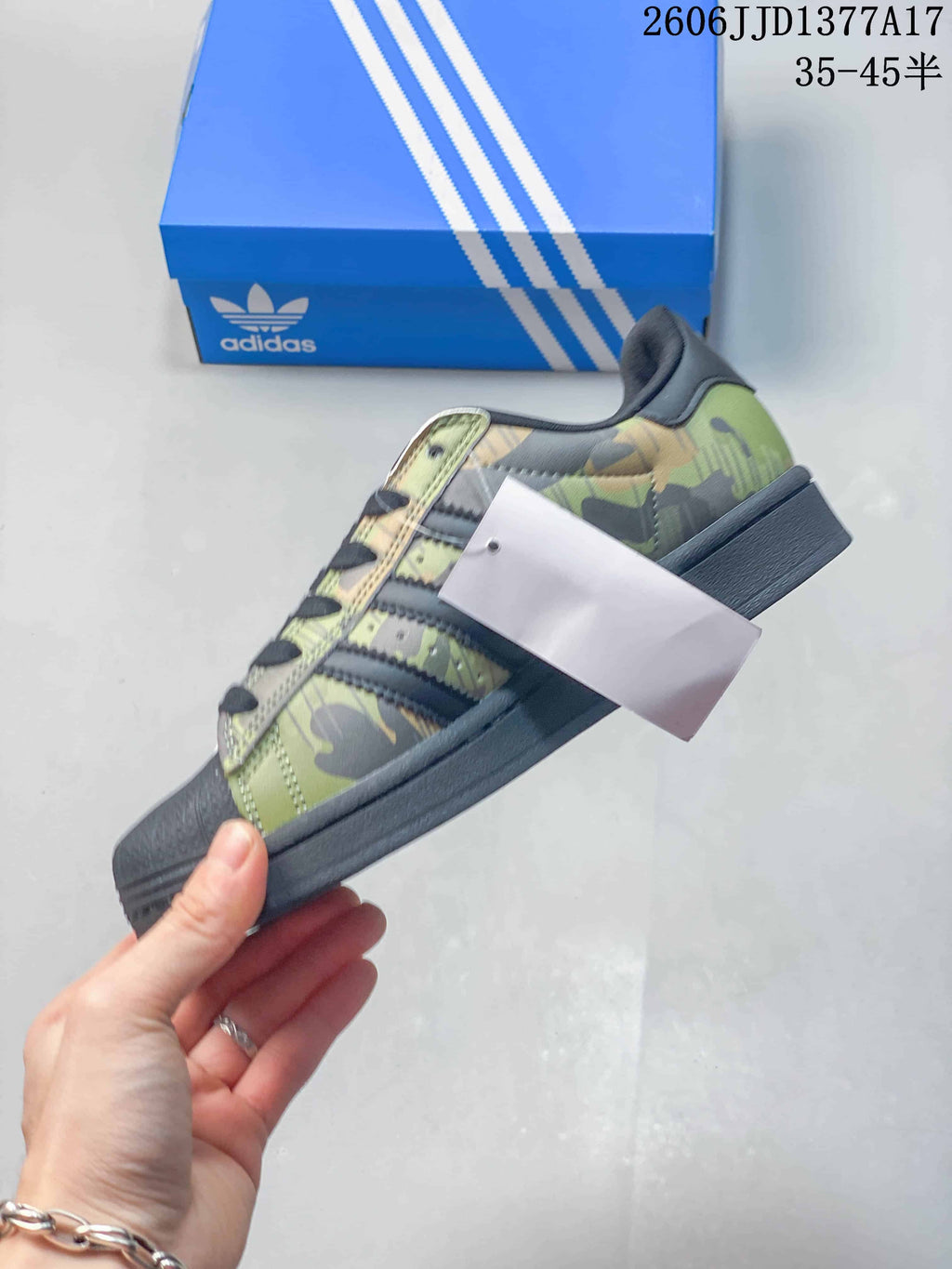 Side view of a camouflage Superstar sneaker with dark stripes, laces, shell toe, and sole