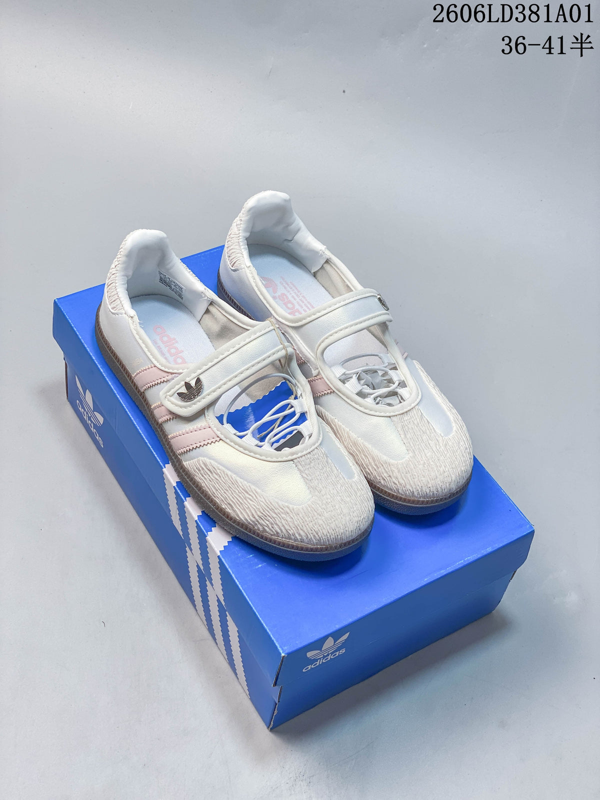 Pair of white Adidas Samba Jane sneakers with pale pink stripes and gum-colored soles, shown on a blue shoe box