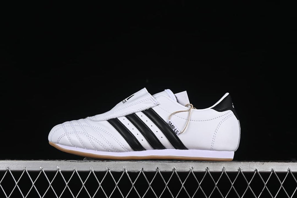 Side view of a white adidas Taekwondo shoe with black stripes and a gum-colored outsole.