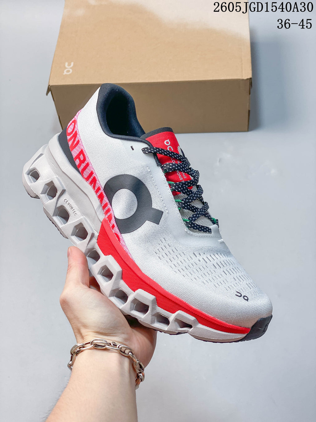 Side view of a white On Cloudmonster 2 shoe with coral-red detailing and a sculpted sole