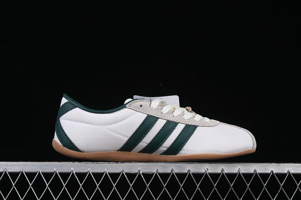 Side profile of a white Adidas Tokyo sneaker with dark green stripes and a gum-colored sole
