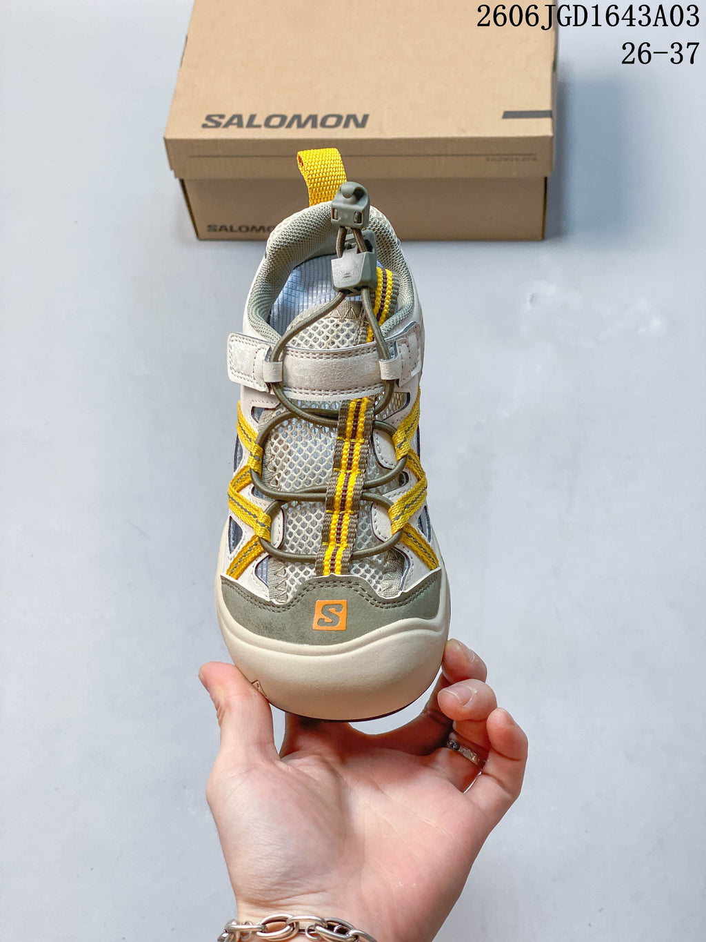 Front view of a beige and gray Salomon kids sneaker with toggle-style laces