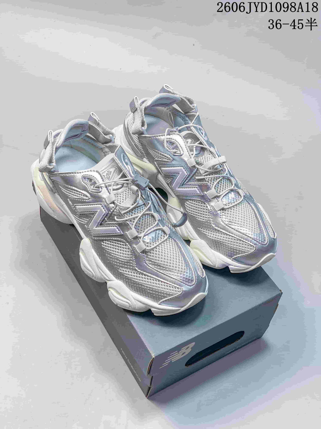 Silver-toned New Balance 9060 sneakers with toggle laces on a shoe box.