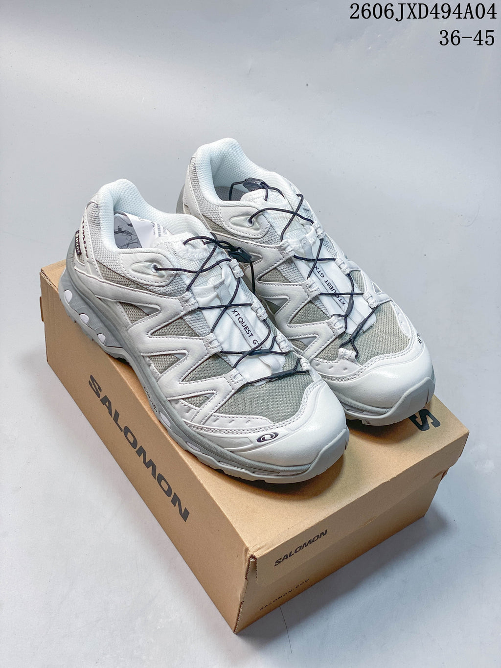 White and gray Salomon XA Pro 3D sneakers with dark quick-lace cords on a shoe box.