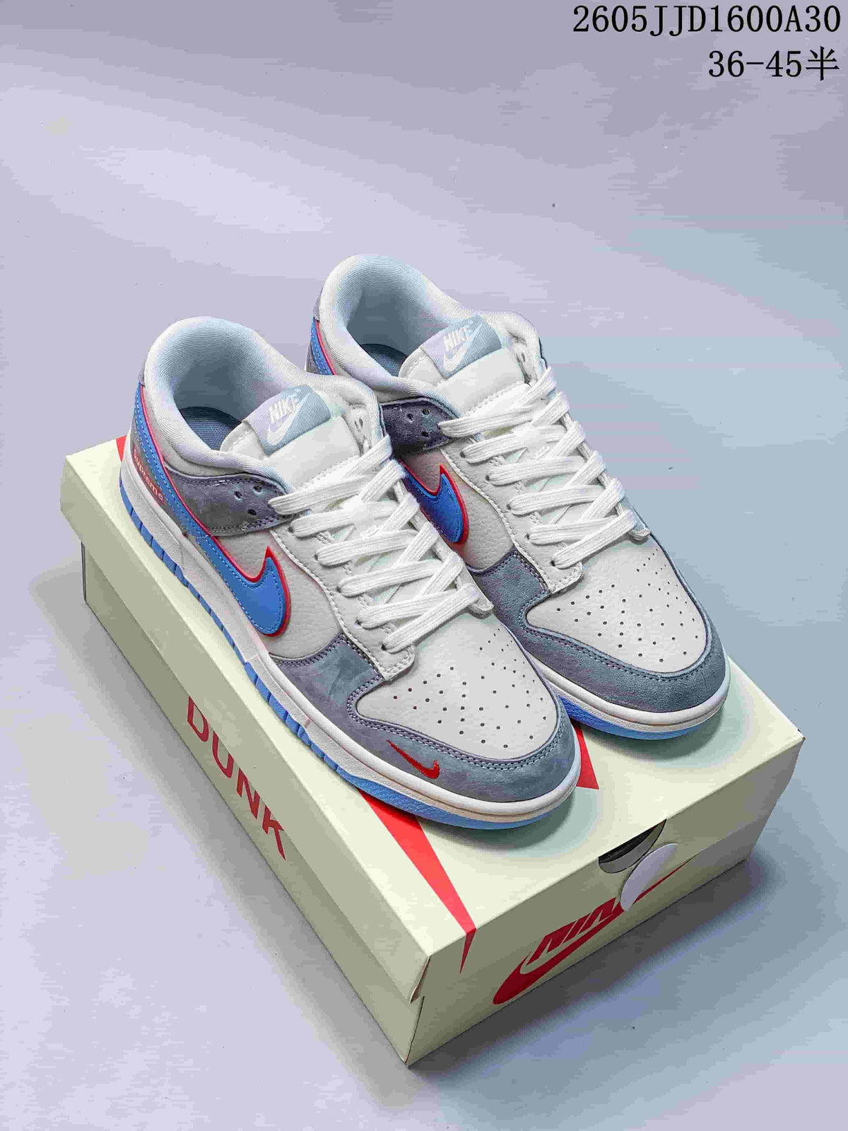 Pair of light grey and off-white Nike SB Dunk Low sneakers with blue and red accents, shown with a shoe box