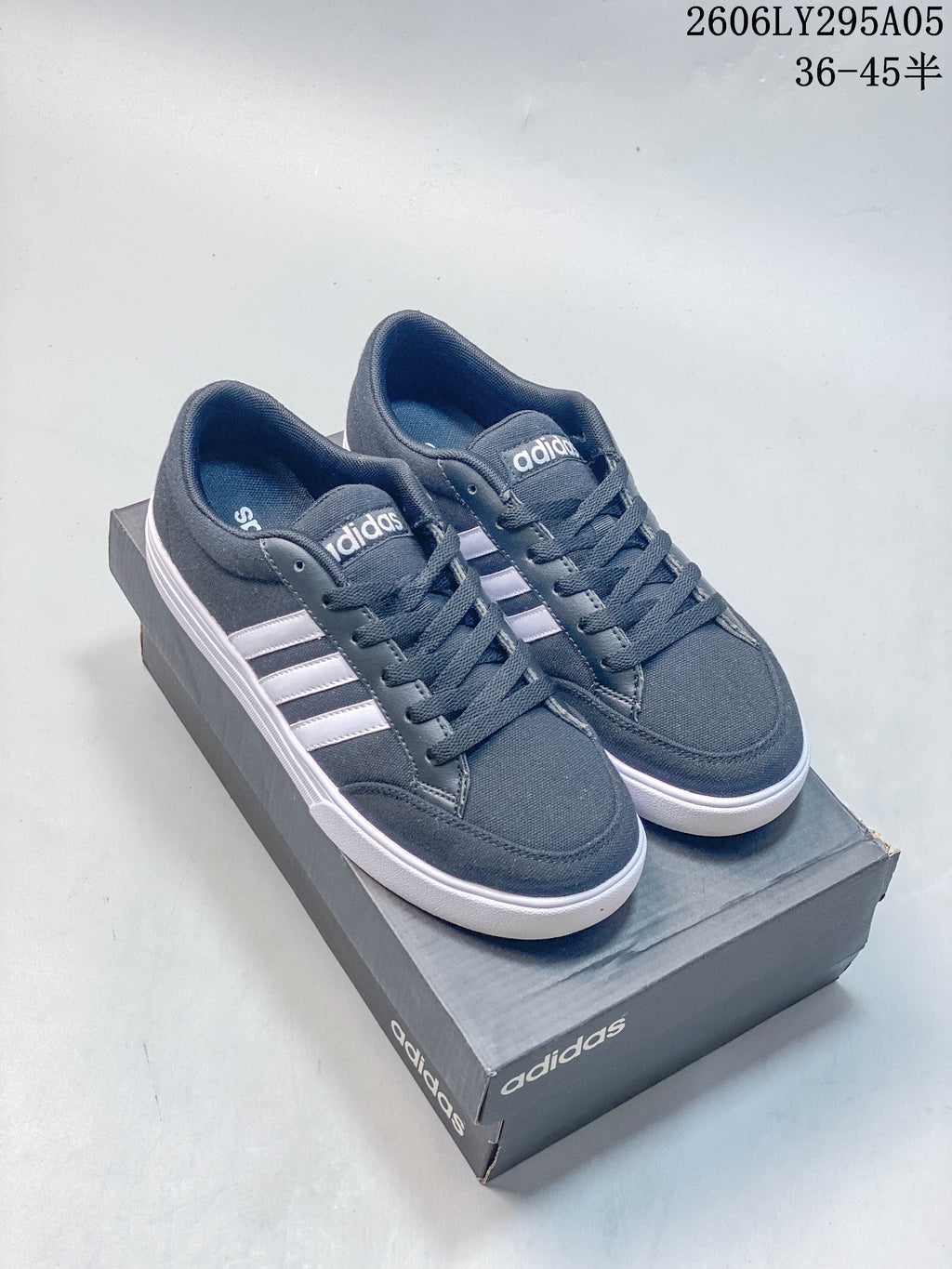 Pair of charcoal gray Adidas low-top sneakers with white side stripes and white outsoles, shown on a shoebox.