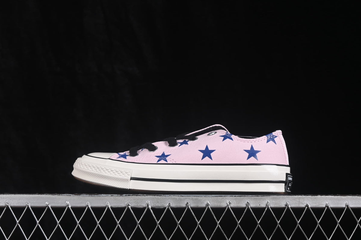 Opposite side view of the pink low-top sneaker with blue star graphics and black-and-white sole detailing.