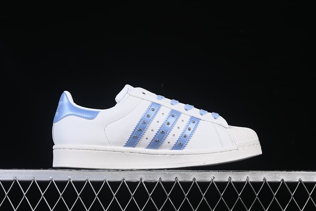 Side profile of a white sneaker with pale blue embellished stripes.