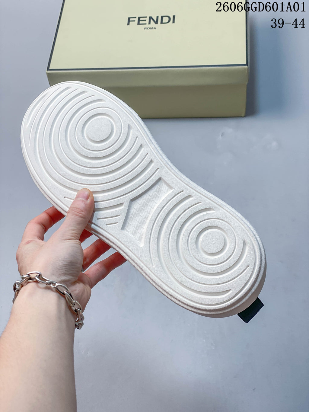 Underside of the white sneaker sole with circular tread patterns; a Fendi shoe box is behind it.