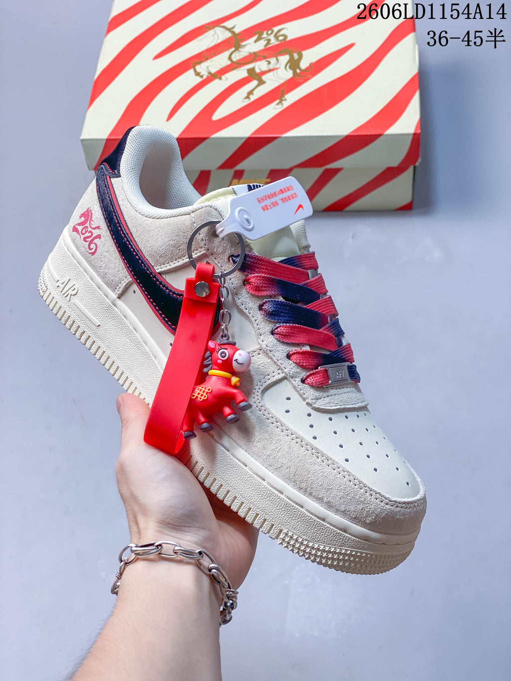 Angled view of a cream sneaker with a navy Swoosh, red accents, and a character keychain