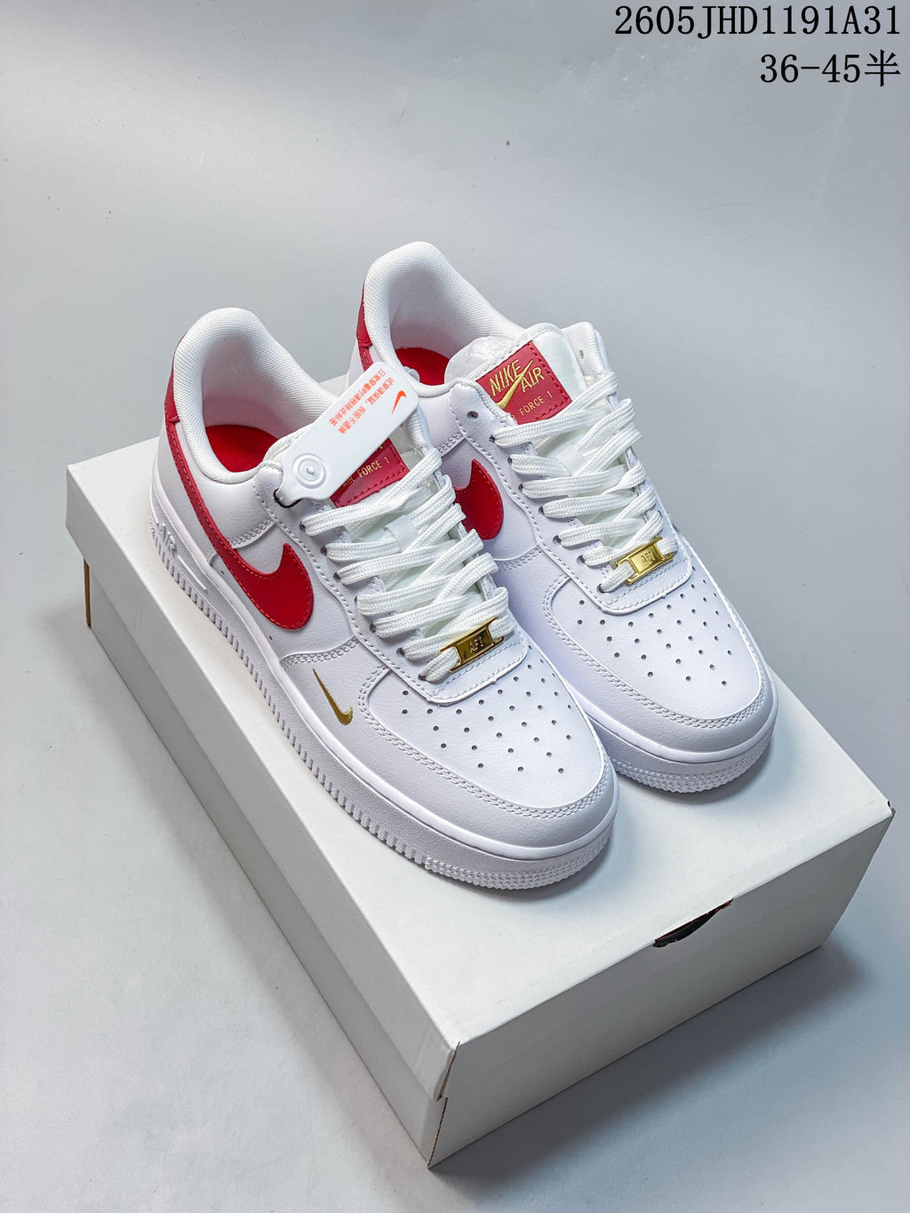 Pair of white low-top Nike Air Force 1 sneakers with red accents and gold-tone lace details