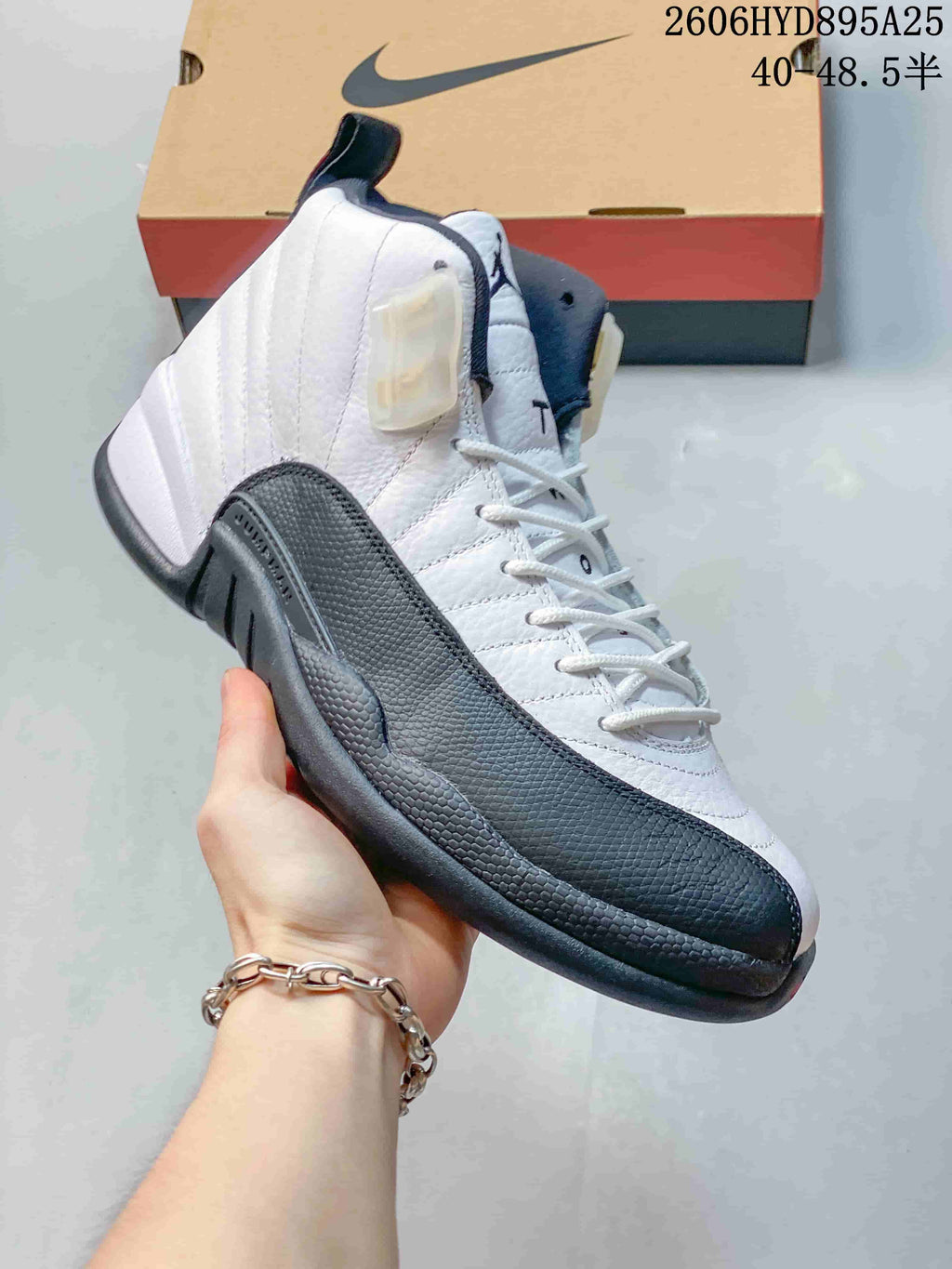Side view of a white and black Jordan Air Jordan 12 high-top shoe, showing textured panels and lace-up closure.